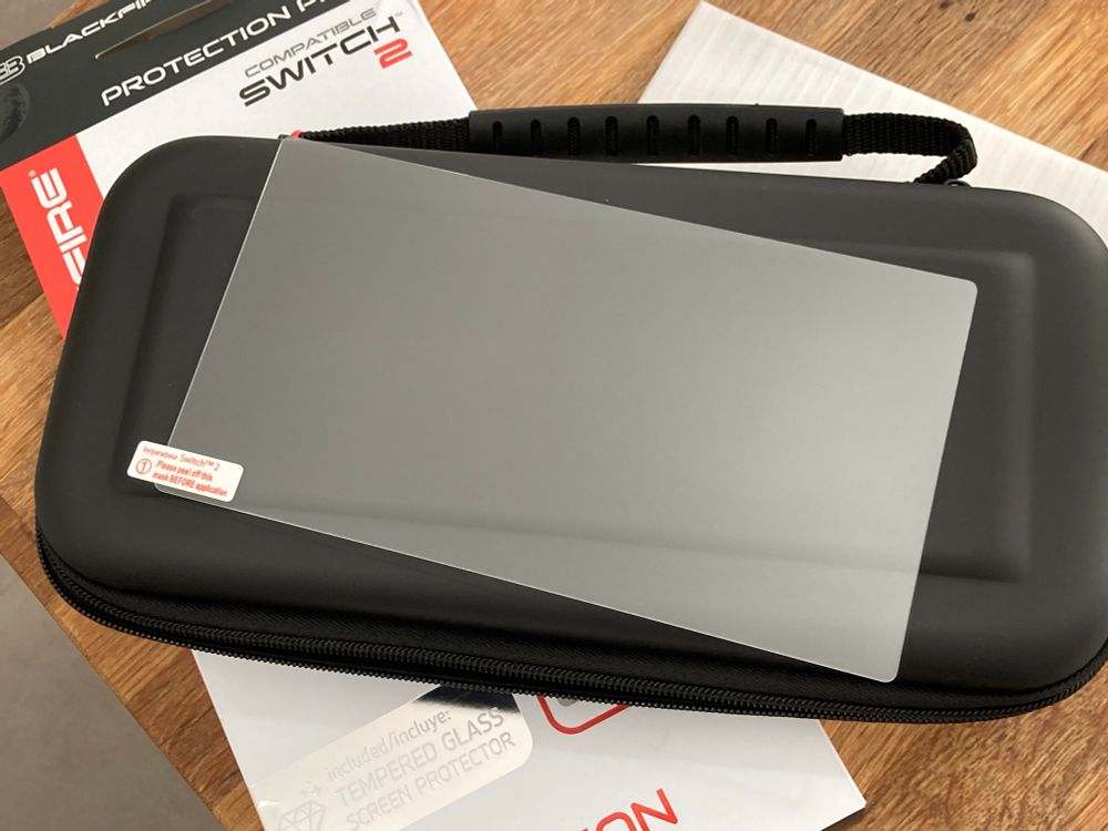 Switch 2 carry case on a table with a Switch 2 screen protector resting on top.