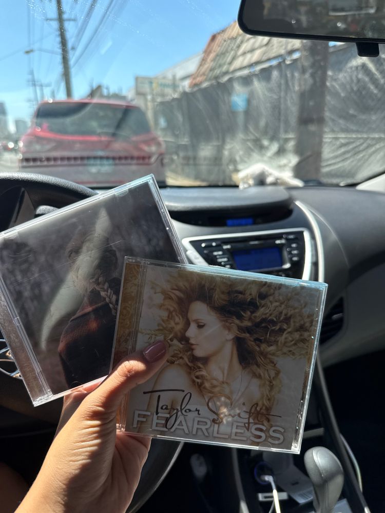 holding cds of evermore and fearless og with a background of a car with cd and radio options only. this bestie is broke in short, like broke broke
