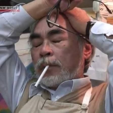 Miyazaki with a cigarette in his mouth and holding his head and glasses looking like he's going through it