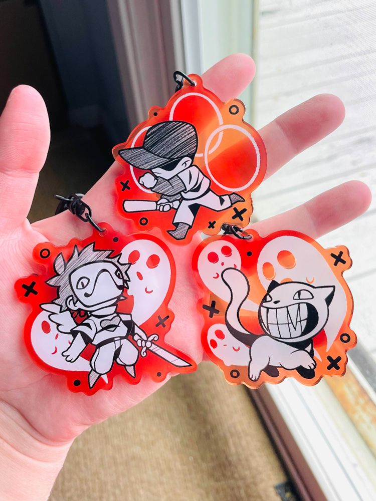 a picture of a hand holding three keychains. the keychains display three characters from off: the batter, the judge, and zacharie
