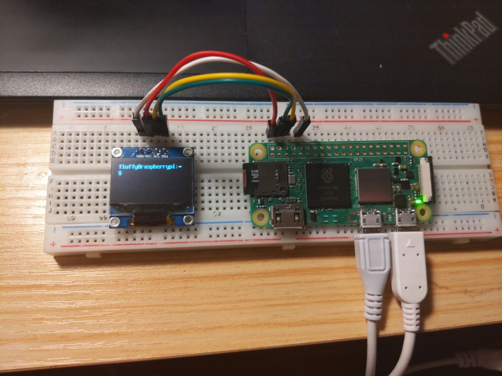 A Raspberry Pi Zero 2W wired up to an SSD1306 OLED screen displaying "fluffy@raspberrypi:~ $" on a breadboard