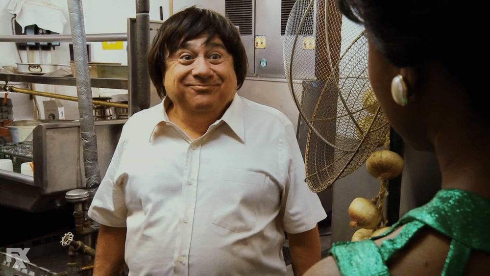 Danny DeVito wearing a wig and a white shirt.