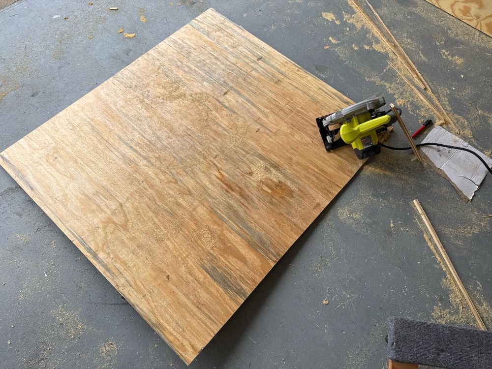 A sheet of plywood and a circular saw sit on a floor