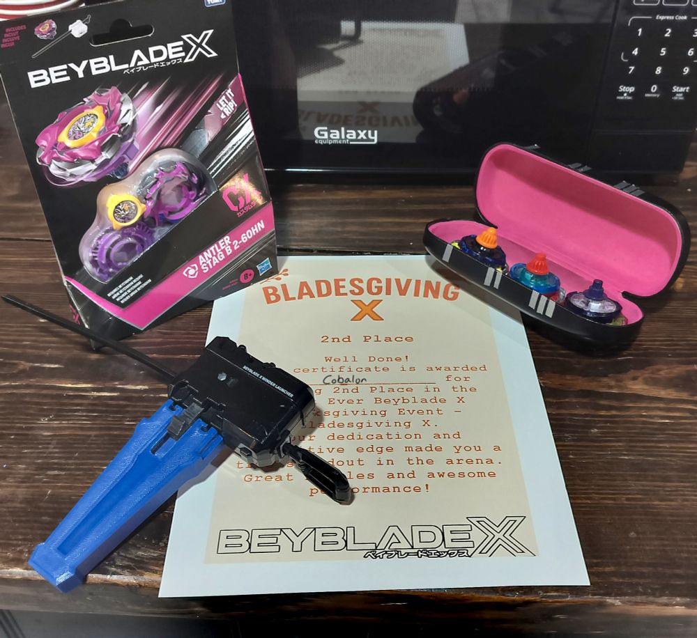 Certificate of 2nd Place placement. Around the certificate are the prize Antler Stag B 2-60HN on the top left, my deck of WizardRod 9-60B, PhoenixWing 3-60LR, and TyrannoBeat 1-60K on the top right, and a black winder launcher with a black ripcord and a blue 3D printer grip on the bottom left.