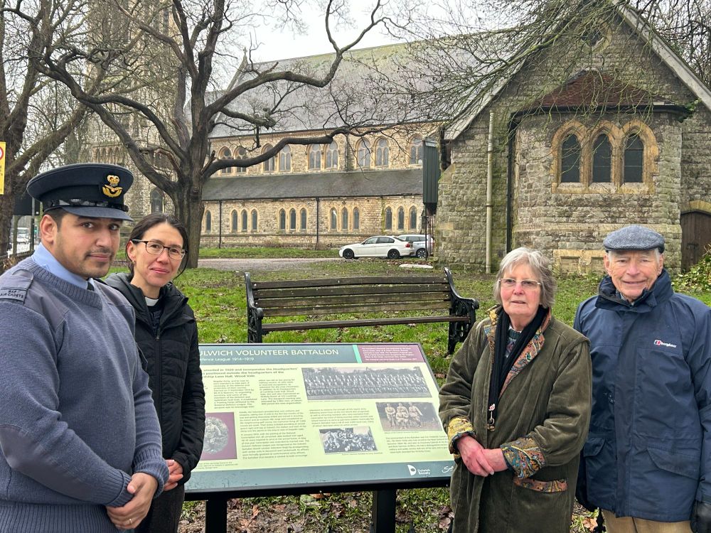 Two men and two women stand beside a new information board about the Dulwich Volunteer Battalion, one is in military uniform, one is a vicar. There is a church in th ebackground.