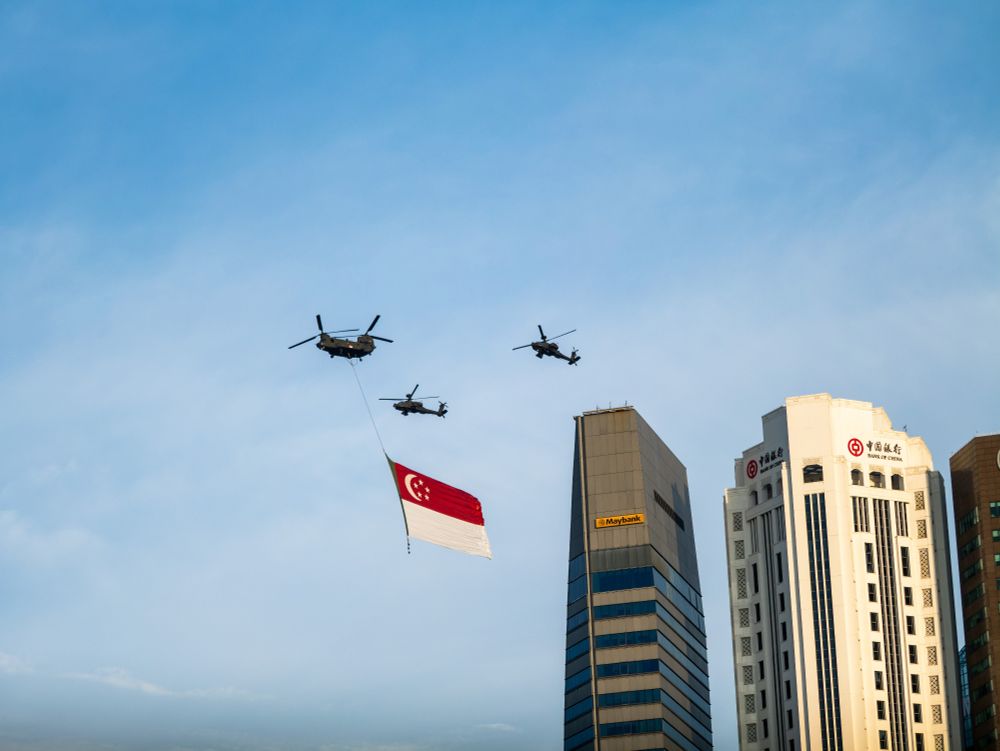 CH-47 Chinook with AH-64D Apache escorts carrying the state flag of Singapore during a flyby near the CBD during National Day Parade preview.