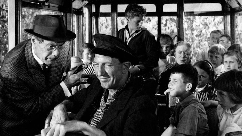 Bilde fra filmen «Bussen» i svarthvit: En mann snakker med en busssjåfør på en buss som er fult av barn