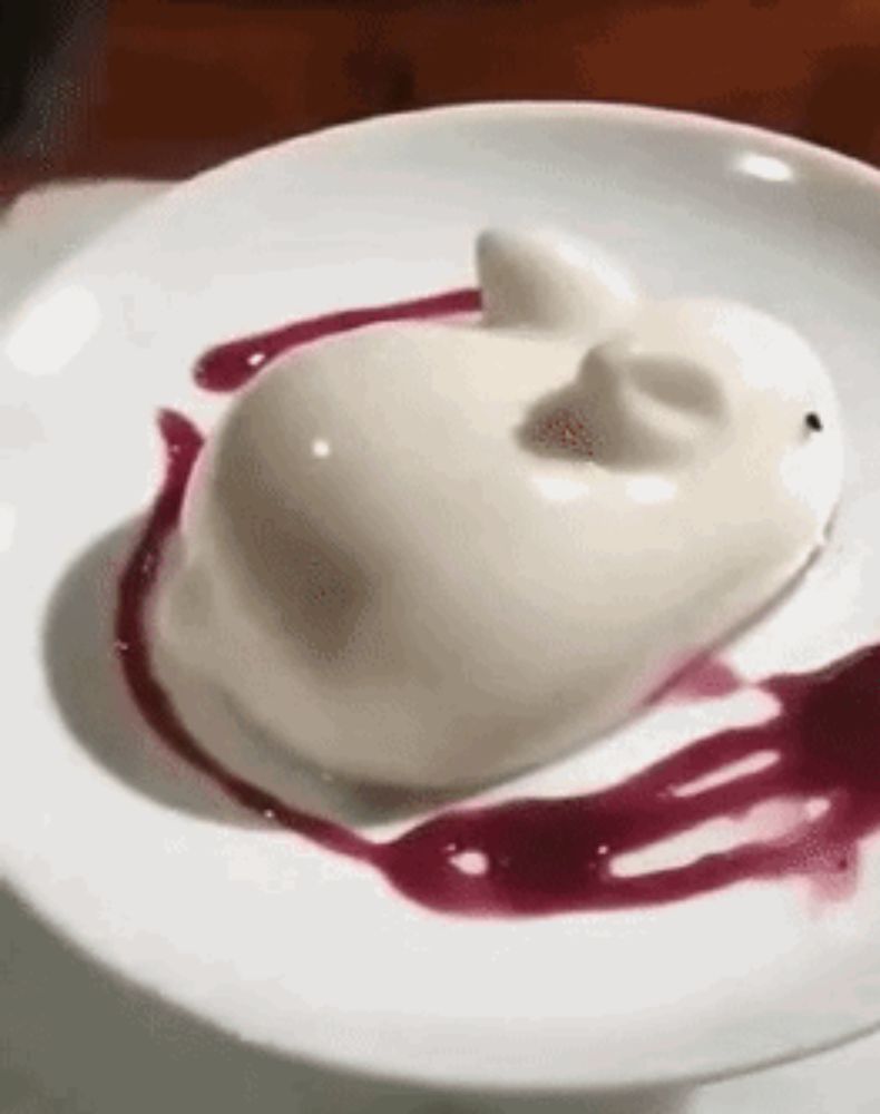 a white dessert in the shape of a cat on a white plate with a purple sauce .