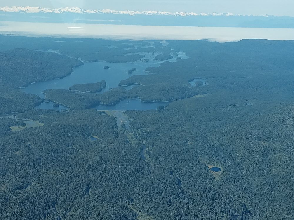 Lakes & inlets of Xootsnoowú (Admiralty Island, Alaska), with Aangóon (Angoon) covered by a marine layer of fog in the distance.
