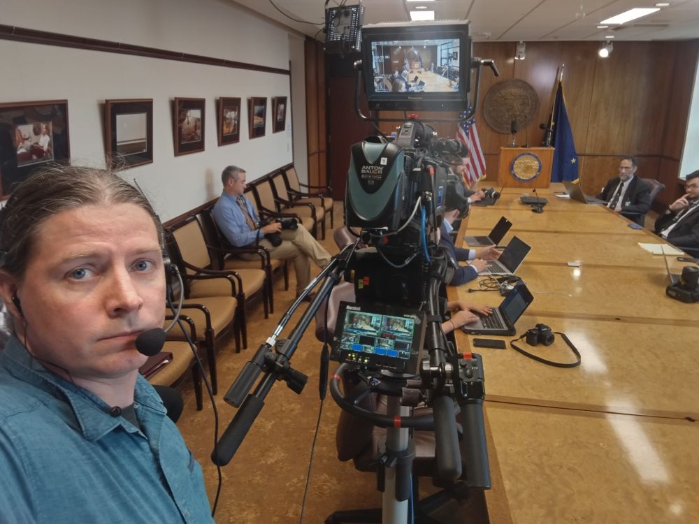 A TV camera operator takes a selfie while waiting for a press conference to begin.