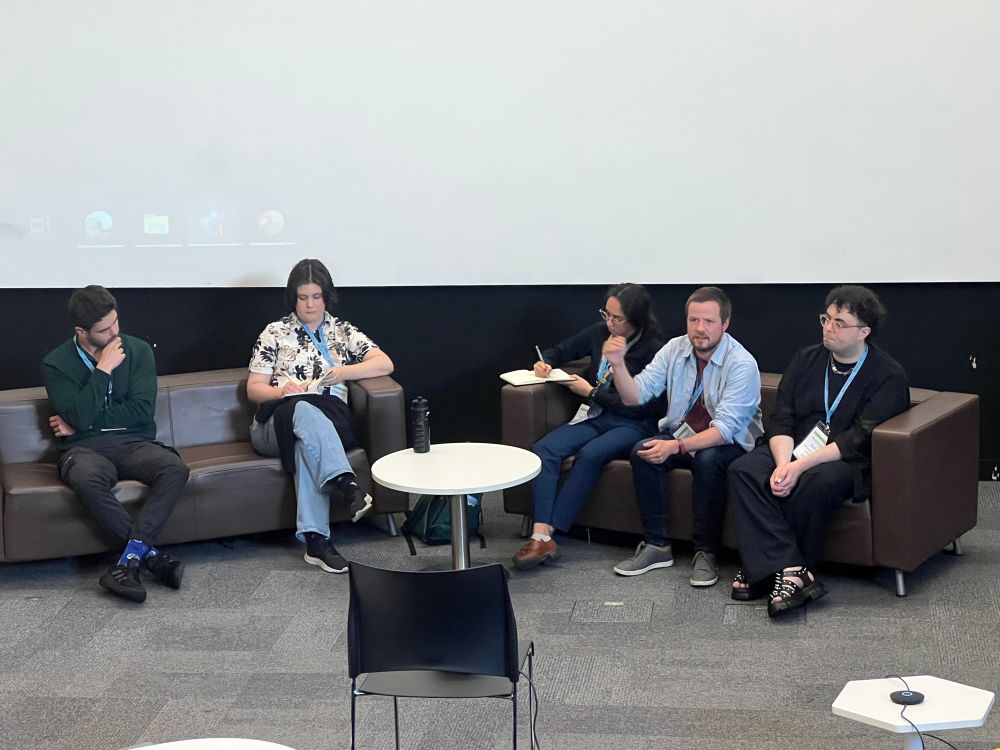 The 5 lightning talk speakers sit on a set of sofas at the front of a lecture theatre 