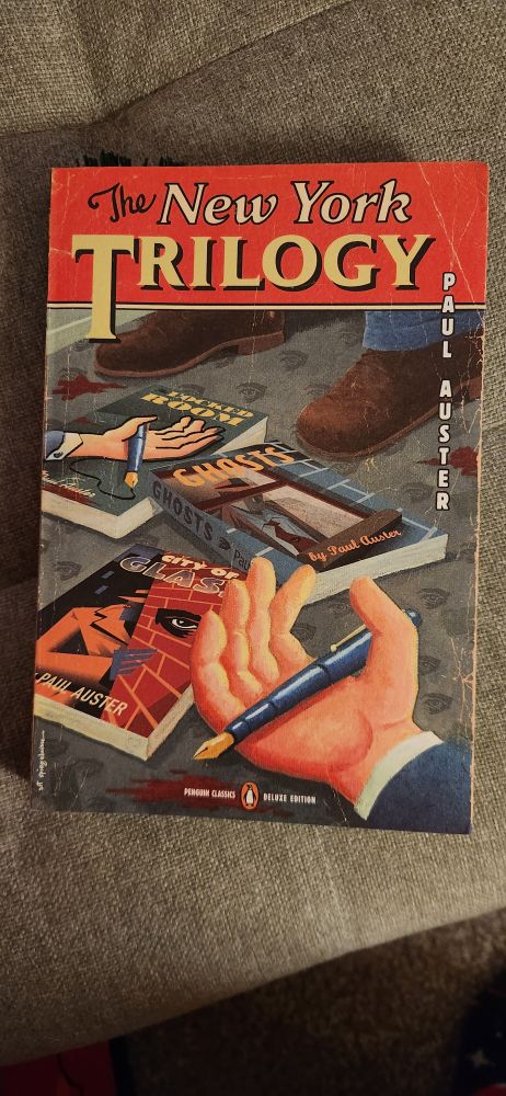 The cover of the book The New York Trilogy by Paul Auster, on which are the covers of the three books within: The Locked Room, Ghosts, and City of Glass.