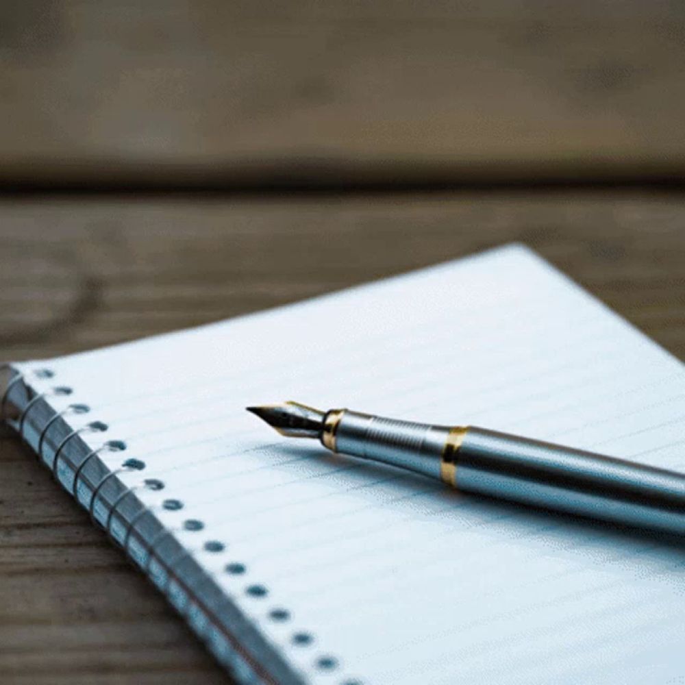 a fountain pen is sitting on top of a spiral notebook