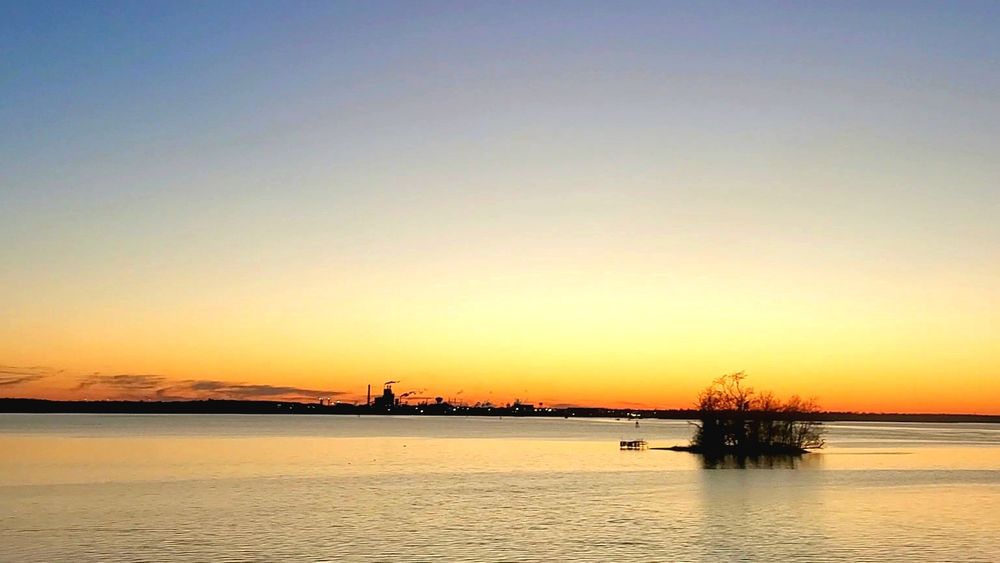 A small island of dark trees in the middle of the James River near Hopewell, Virginia. In the background, massive but distant factories against a brilliant late sunset.