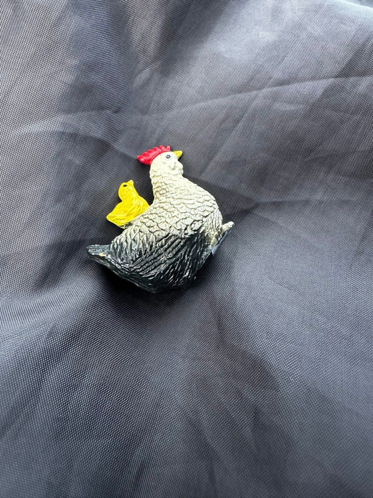 A small plastic tchotchke or toy rooster with a yellow chick on its back. 
