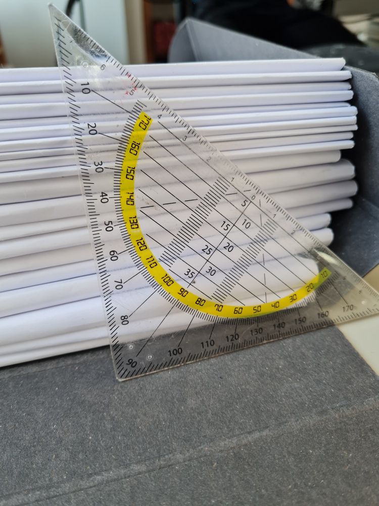 Ein großer Stapel an Klausuren. Zum Größenvergleich liegt ein Geodreick daneben. Der Stapel ist so hoch wie eine Kante lang ist.