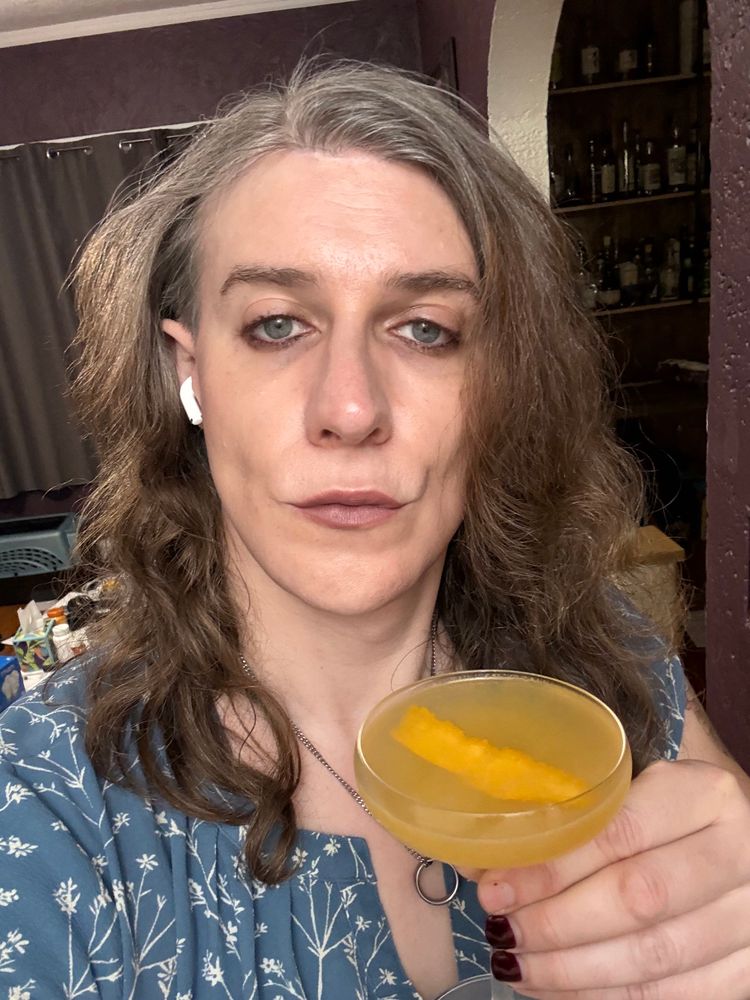 A Maggie holding a coupe glass with yellow orange liquid. 