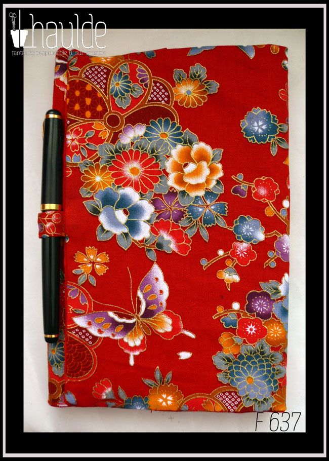 Protège carnet en tissu rouge imprimé fleurs et papillons d'esthétique japonaise. Vu fermé avec un stylo dans l'anneau situé sur le bord du rabat