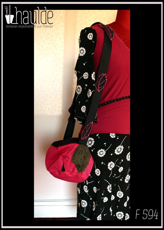 sac boule à bandoulière, vu suspendu à l'épaule d'un mannequin de couture Fond rose fuchsia, dessus et bandoulière en sergé noir Bandoulière garnie de feuilles de sergé noir à nervures rose, feuilles en velours cotelé kaki plaquée sur le sac