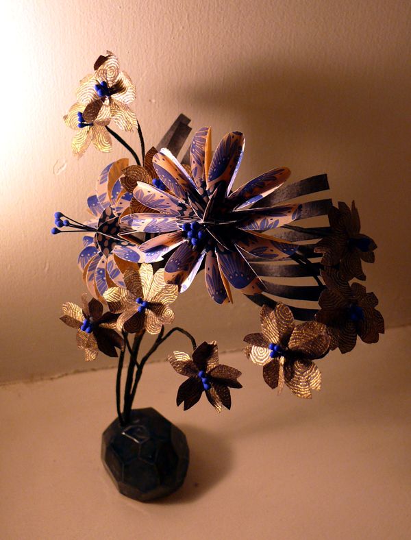 Bouquet de fleurs en papier plié, dans les tons bleu roi et or, leurs tiges sont plantées dans une forme abstraite en céramique émaillée