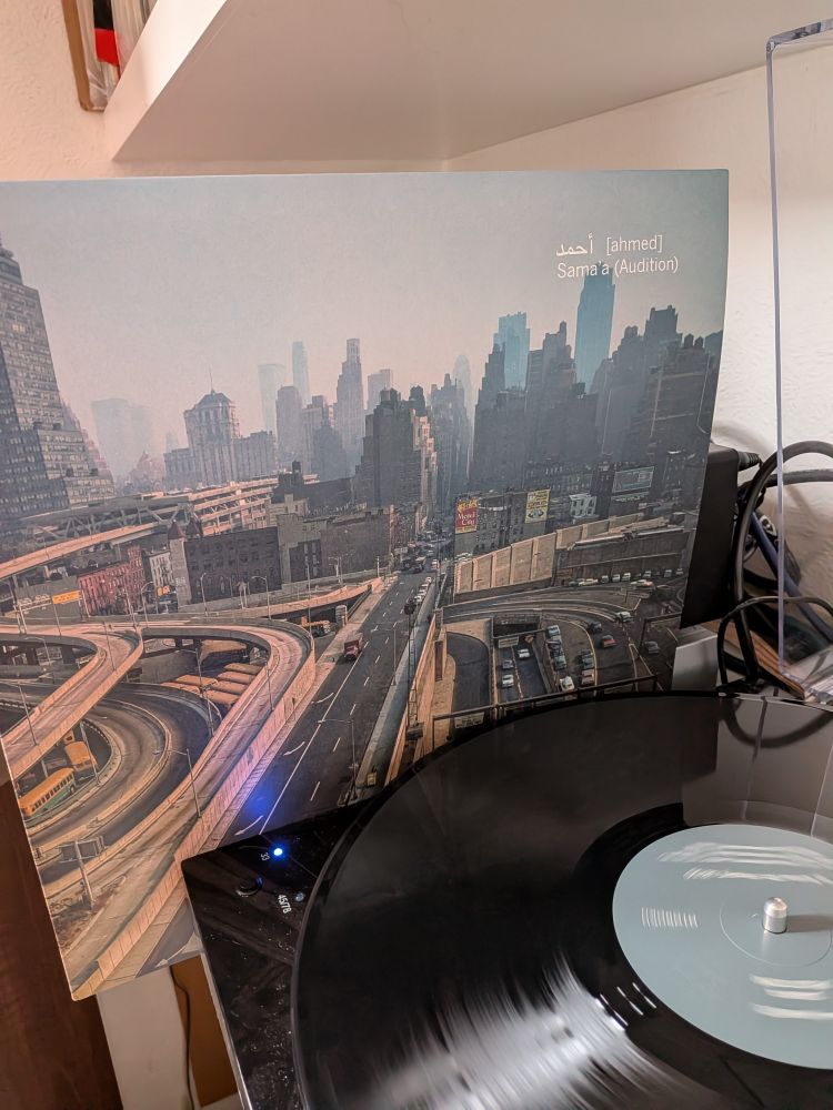 Picture of the LP cover for Sama'a (Audition) by أحمد Ahmed, standing next to the LP playing on a turntable