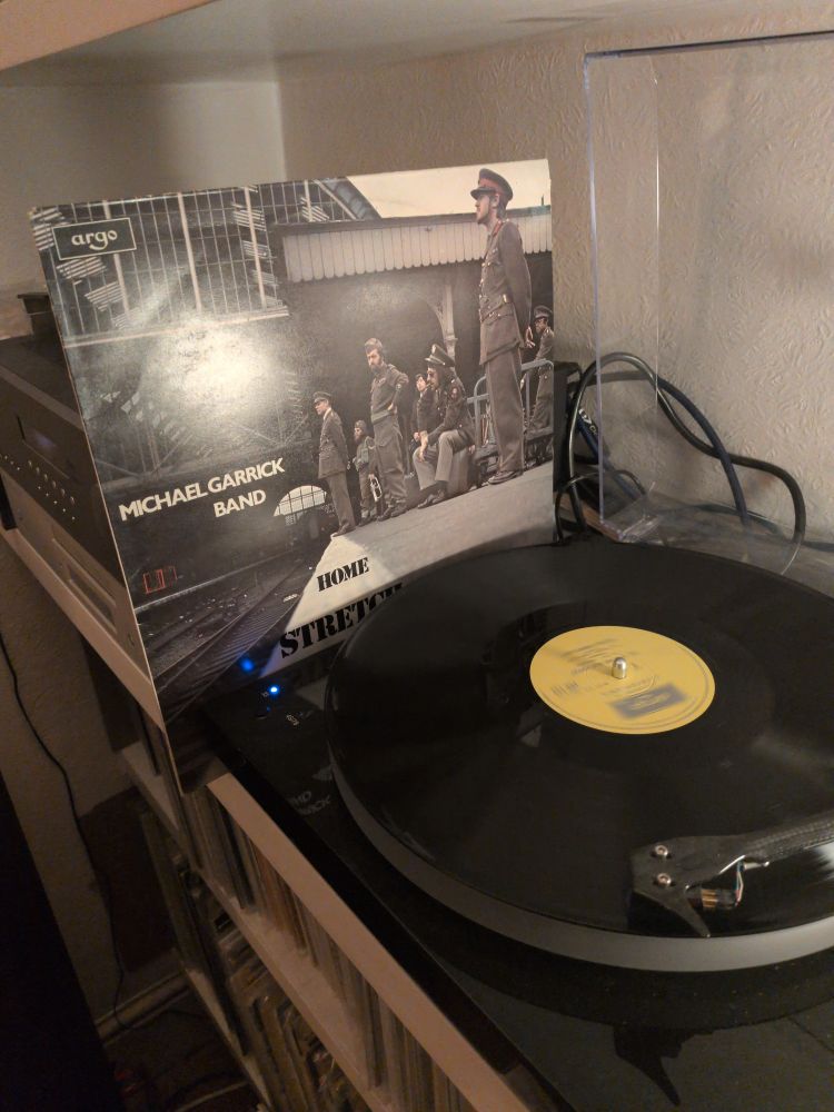 Picture of the LP cover for 'Home Stretch Blues' by Michael Garrick Band standing next to the LP on a turntable 