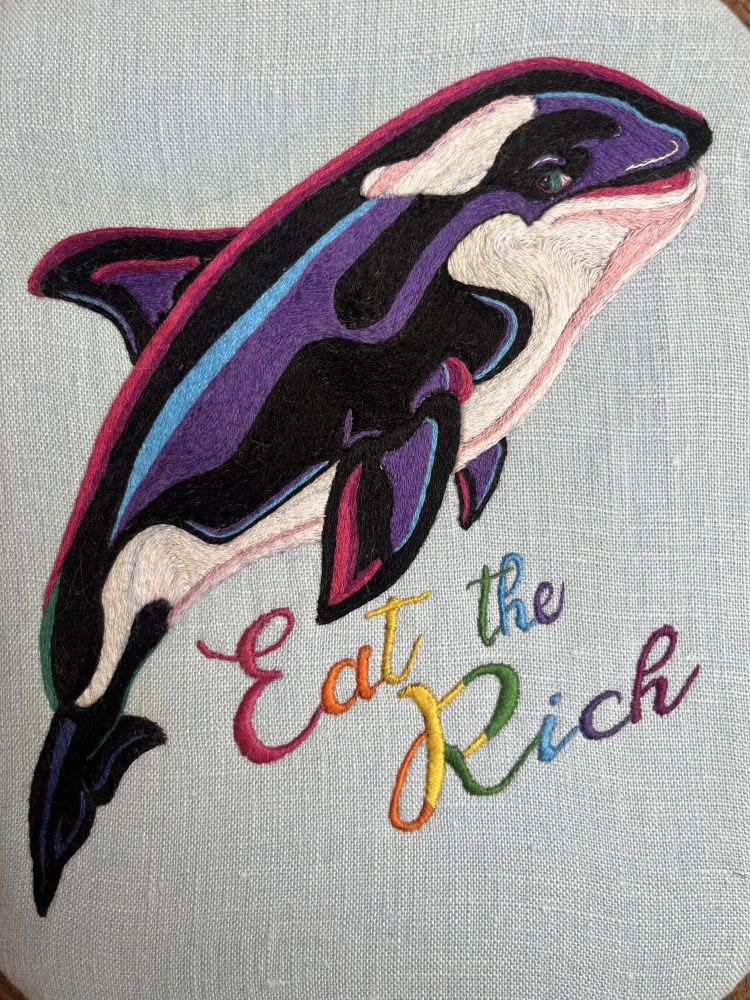embroidery of an orca leaping over the words "Eat the Rich" in rainbow-colored script