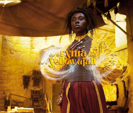 Ryma Sedai of the Yellow Ajah making graceful weaves rotating one hand over another, almost like a dance. She is a beautiful Black woman with natural hair in an updo wearing a long sleeved yellow blouse, a brown vest, a deep red skirt and a serene expression while she prepares to kick ass. Text overlay reads she’s Ryma and she’s Yellow Ajah.