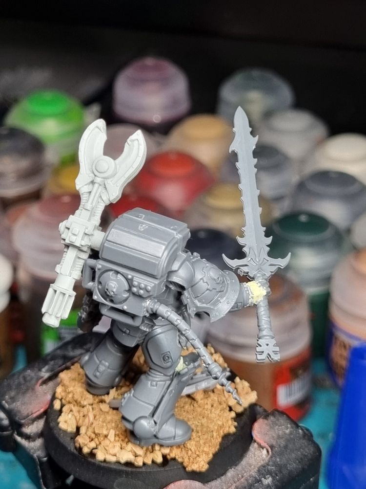 A Techmarine stands holding a daemon weapon, contemplating it. Could it be used for the good of the Imperium? (Rear view) 