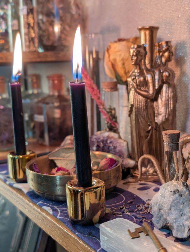 A Hekate altar with multiple black candles, a brass offering bowl, Hekate triformis statuette, crystals, keys, and other ritual items