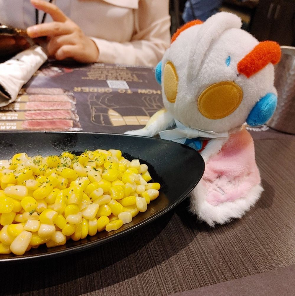 photo of an Ultraman X fuwafuwa. he is looking at a plate of corn at a restaurant while wearing a cape.