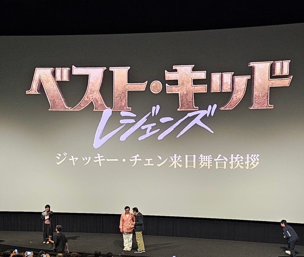 新宿TOHOシネマでスクリーンを背に通訳の人と並んで舞台に立つジャッキー・チェン