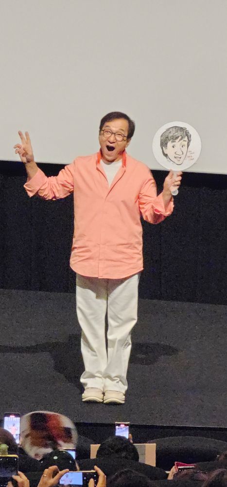 ファンが自作した似顔絵のうちわを手にして嬉しそうにおどけ顔でピースをするジャッキー・チェン