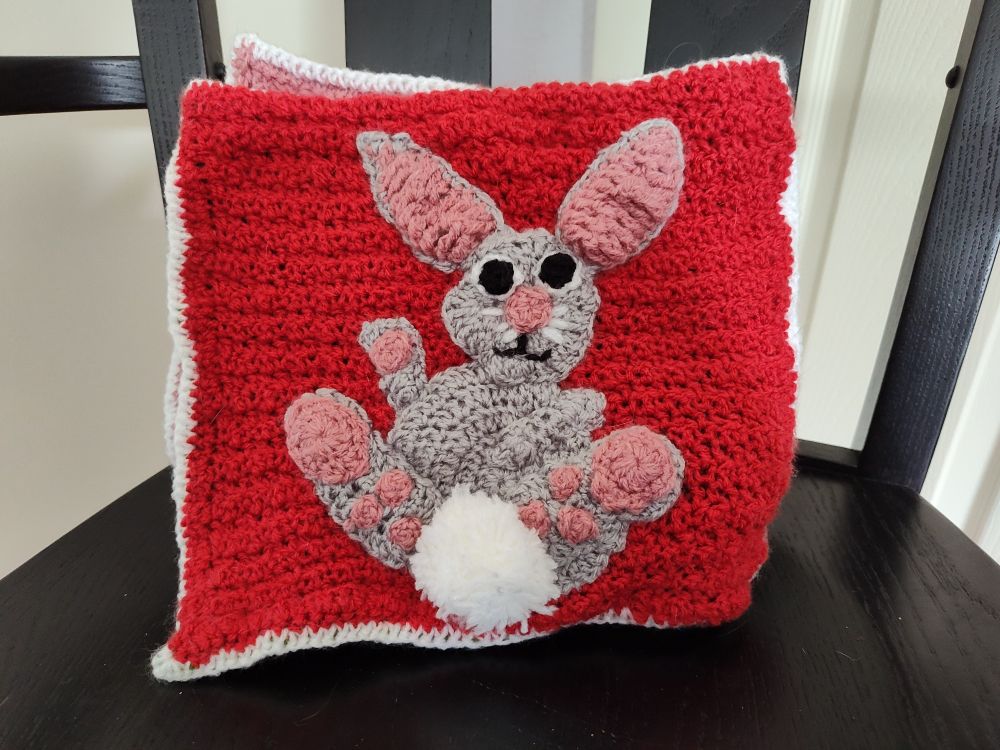 Gray bunny on a red background.  The bunny has pink on its ears and feet and a fluffy white tail