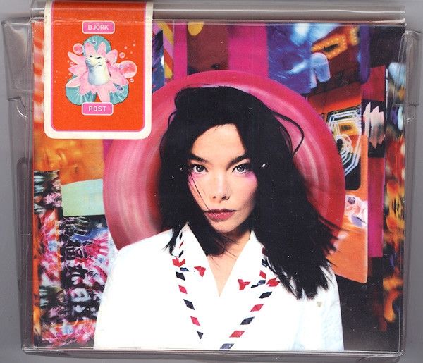 Cover of a cd called Post by Björk. Björk is a dark haired woman, standing in from of a colourful decor with lots of orange and pink. She is wearing a white jacket that looks like it was made of airmail envelopes.