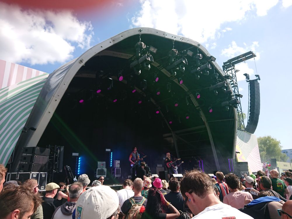 Smaller festival stage with a band playing and lots of people in front of it.