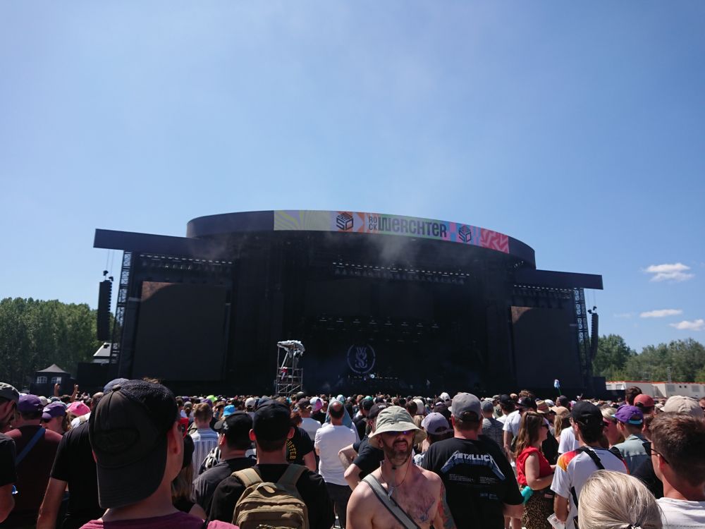 Big festival stage on a sunny day with a big crowd.