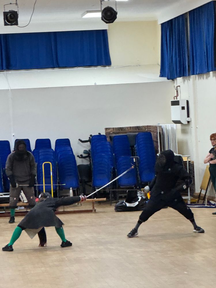 Two fencers dressed in dark clothing fencing with rapiers 