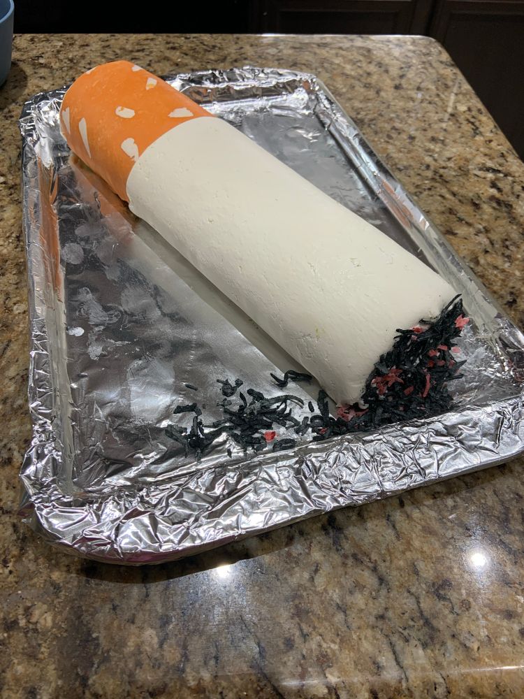 A long roll cake decorated with modeling chocolate to look like a cigarette. This is a different angle showing fake ash at the tip. 
