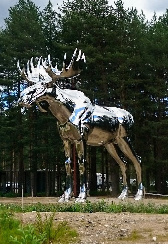 A huge statue of a silver plated moose. Trees in the background.