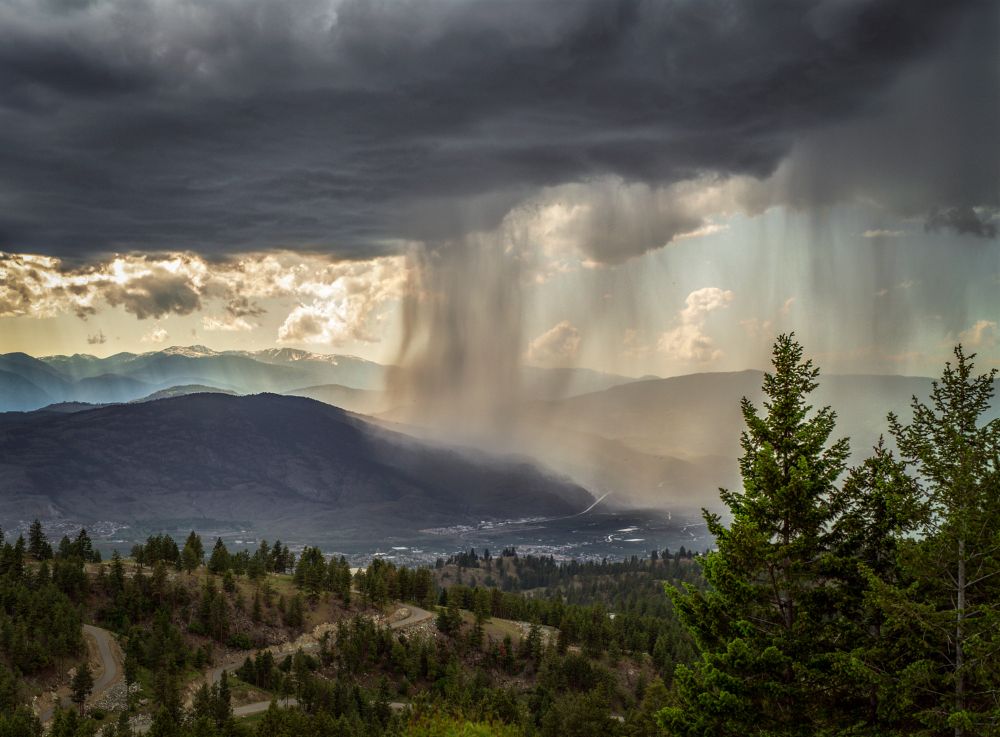 dark clouds releasing sheets of rain over valley surrounded by mountains