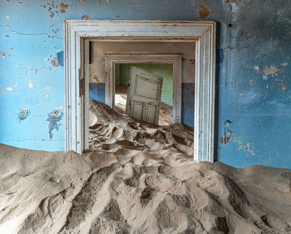 Kolmanskopp, Namibia, Africa. an old abandoned mining town where the desert is taking over the buildings. A house filled with desert sand. The house still has brightly colored wallpaper, door buried in sand.