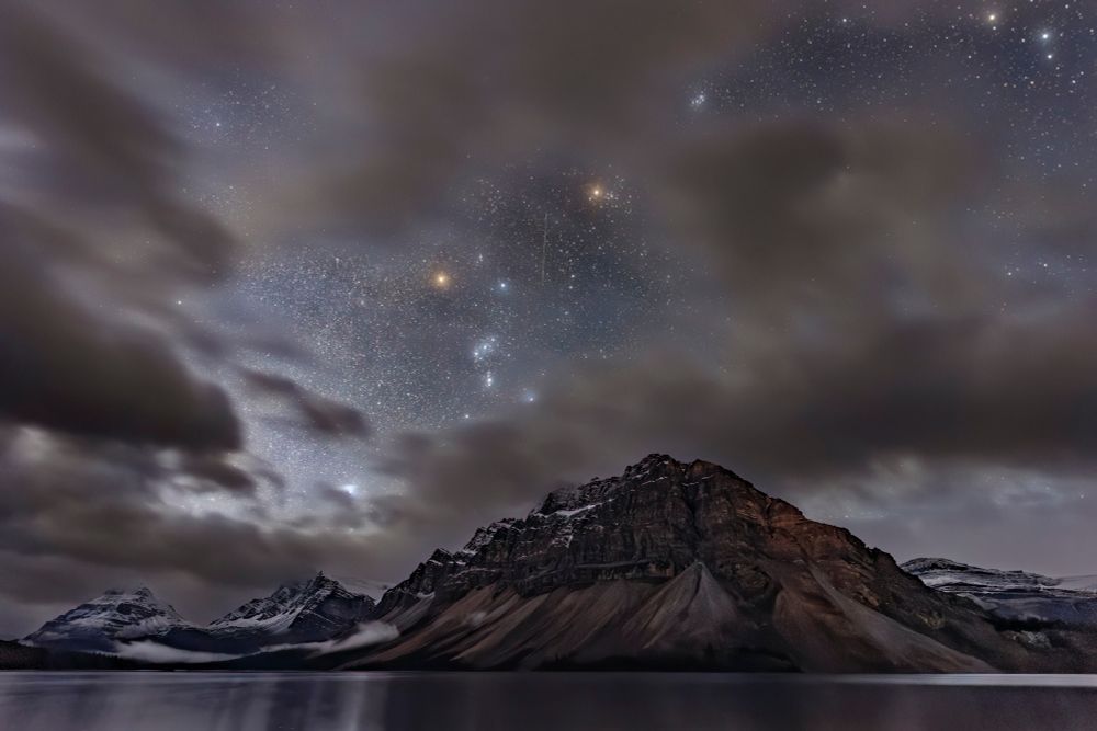 The constellation of Orion through clouds over Bow Lake and mountain, Banff National Park, Alberta, Canada