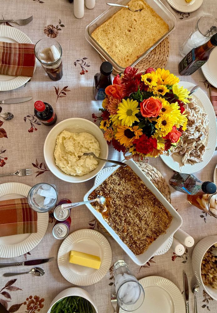 Overhead photo of a table with turkey, Thanksgiving sides, and a bouquet of flowers. 