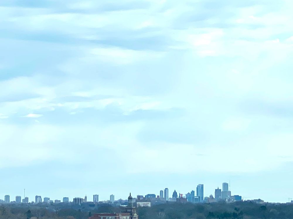 The Milwaukee skyline on a low horizon with a towering impressionistic sky, all thin white clouds with patches of blue, pale, pale blue. 