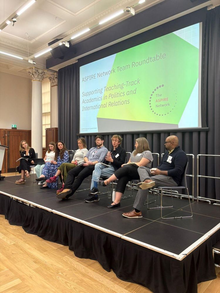 Image of 8 people on a stage in front of a slide saying "supporting teaching track academics in politics and international relations" 