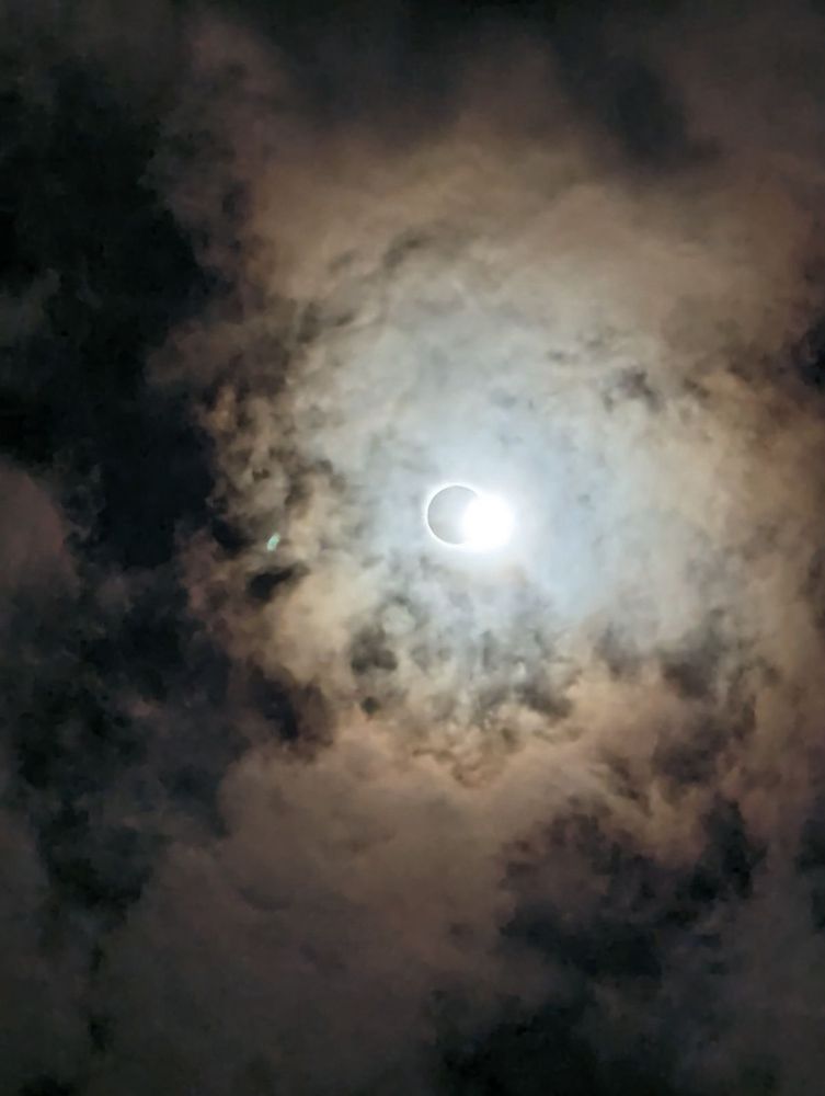 A sun in almost total eclipse through clouds. 