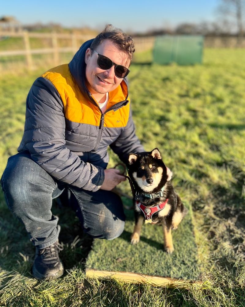 Man and Black and Tan Shiba Inu puppy in a field of grass