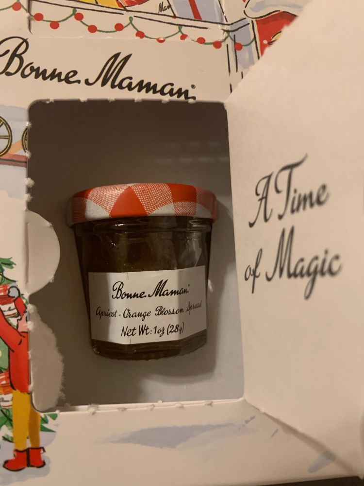 A little jar of jam inside an advent window; on the inside of the door it says “A Time of Magic”
