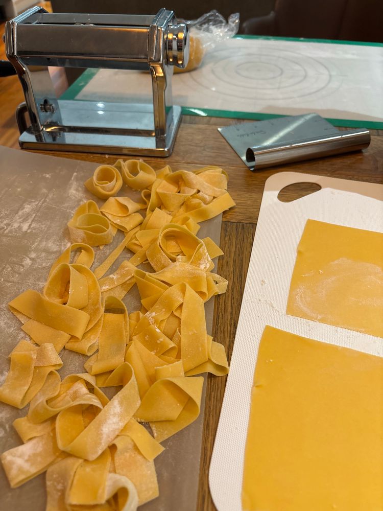 Process photo: a manual pasta machine, some flat sheets of pasta, and some cut and swirled wide pappardelle noodles. Not shown: blood, sweat and tears. 